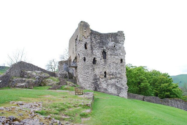 A stone ruin with a bench in a grassy field.