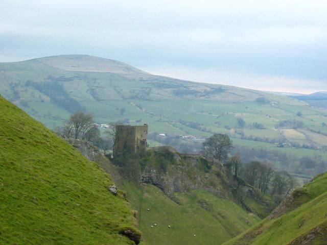A castle on a hill with rolling green hills and a cloudy sky in the background.