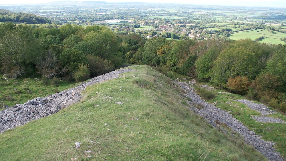 Ein grasbewachsener Hügel mit einer Steinsäule und Blick auf eine Stadt in der Ferne.