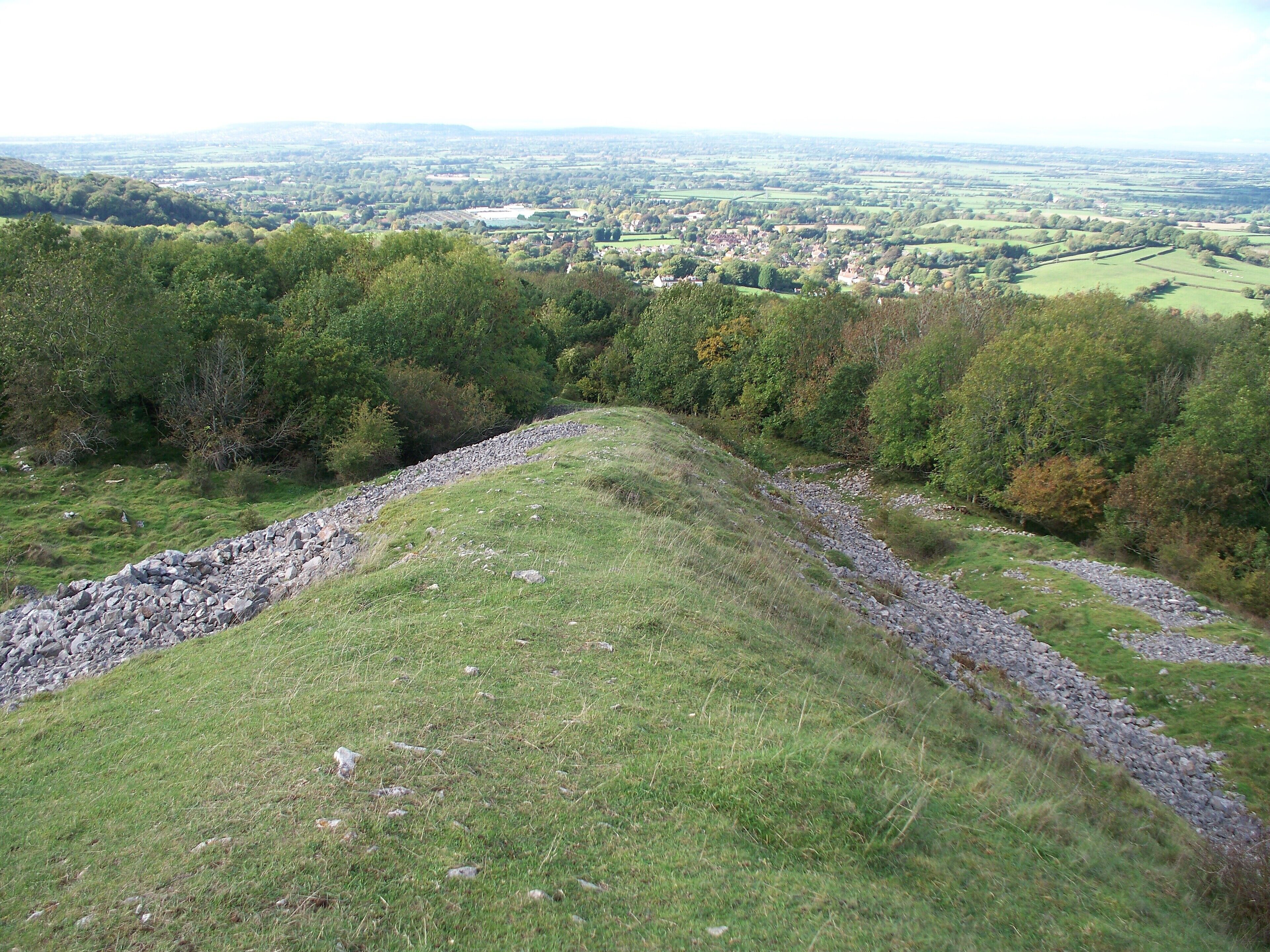 A grassy hill with a stone wall and a view of a town in the distance.