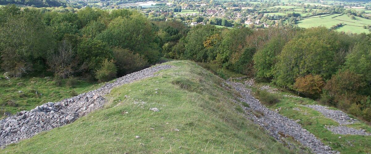 A grassy hill with a stone wall and a view of a town in the distance.