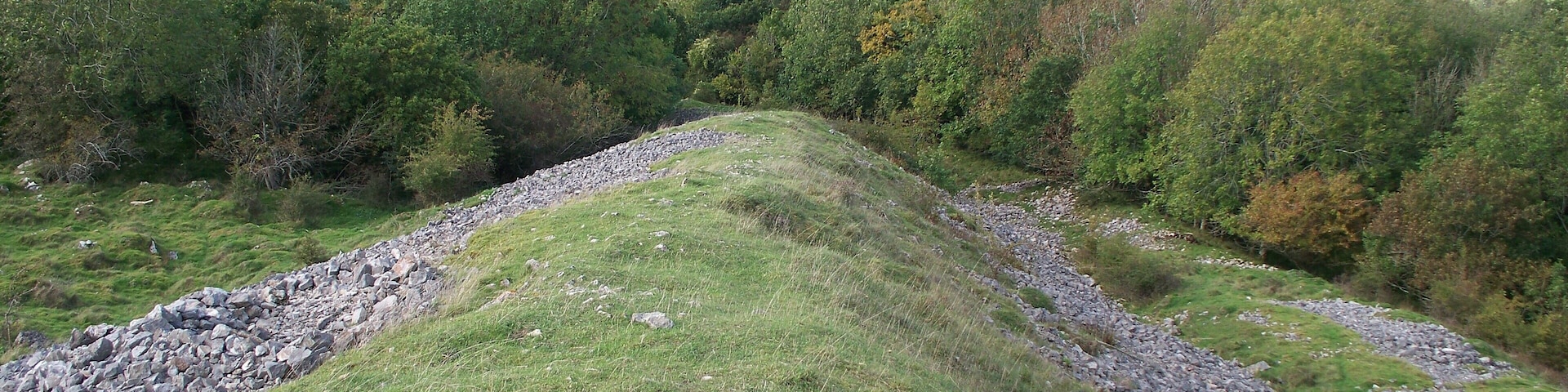 A grassy hill with a stone wall and a view of a town in the distance.