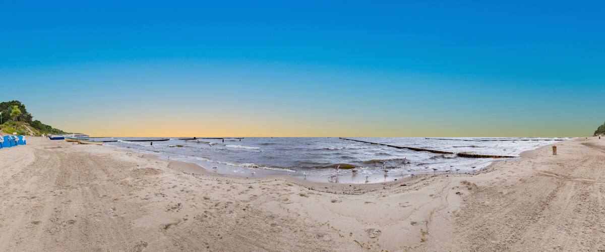 A beach with a calm sea, a sandy shore, and a pier extending into the water.