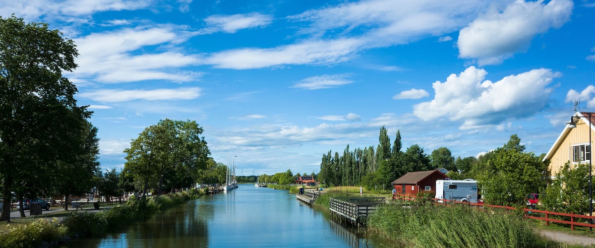A calm river with a wooden bridge, houses, and trees along the banks.