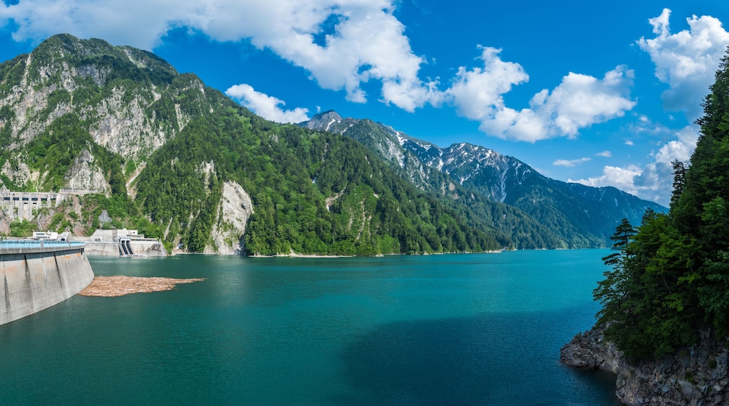 Panorama Beautiful scenery of Kurobe Dam on a brisk, with colorful lakeside mountains and crystal clear lake water under blue sunny sky in Tateyama Kurobe Alpine Route, Toyama, Japan
