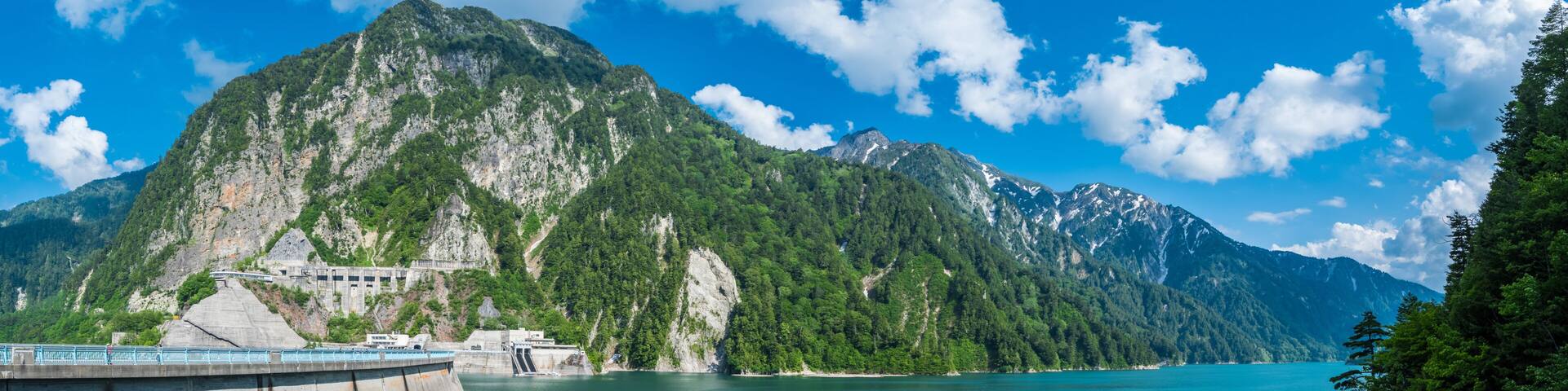Panorama Beautiful scenery of Kurobe Dam on a brisk, with colorful lakeside mountains and crystal clear lake water under blue sunny sky in Tateyama Kurobe Alpine Route, Toyama, Japan