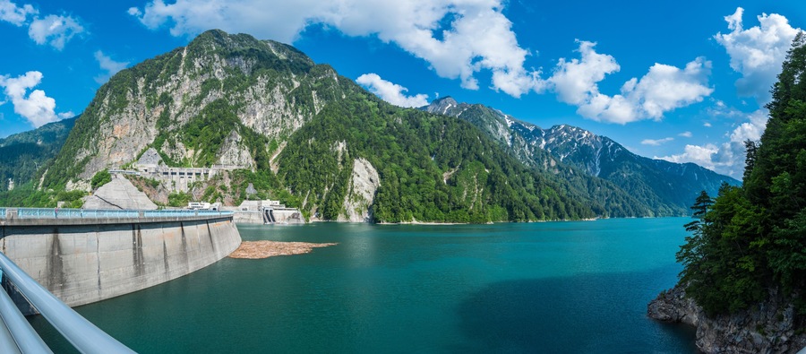 Panorama Beautiful scenery of Kurobe Dam on a brisk, with colorful lakeside mountains and crystal clear lake water under blue sunny sky in Tateyama Kurobe Alpine Route, Toyama, Japan