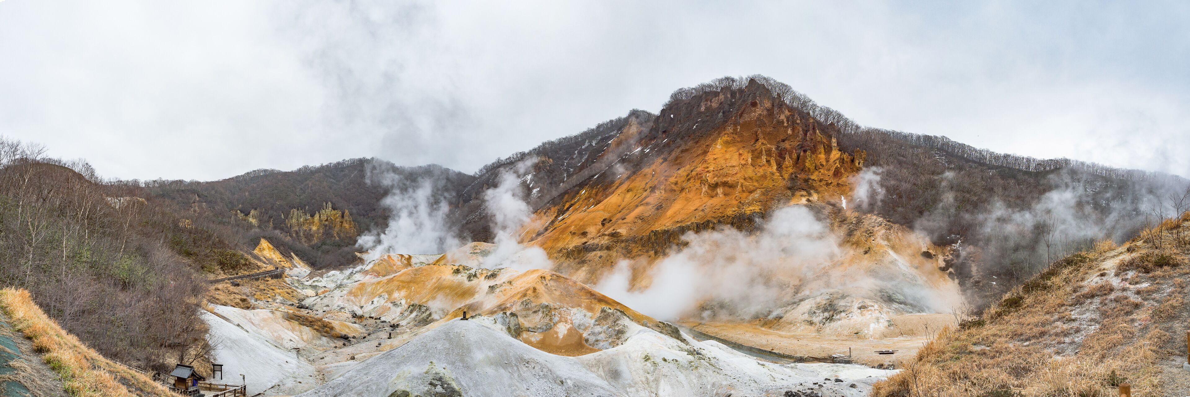 A geothermal area with steam vents, mineral deposits, and a wooden viewing platform.