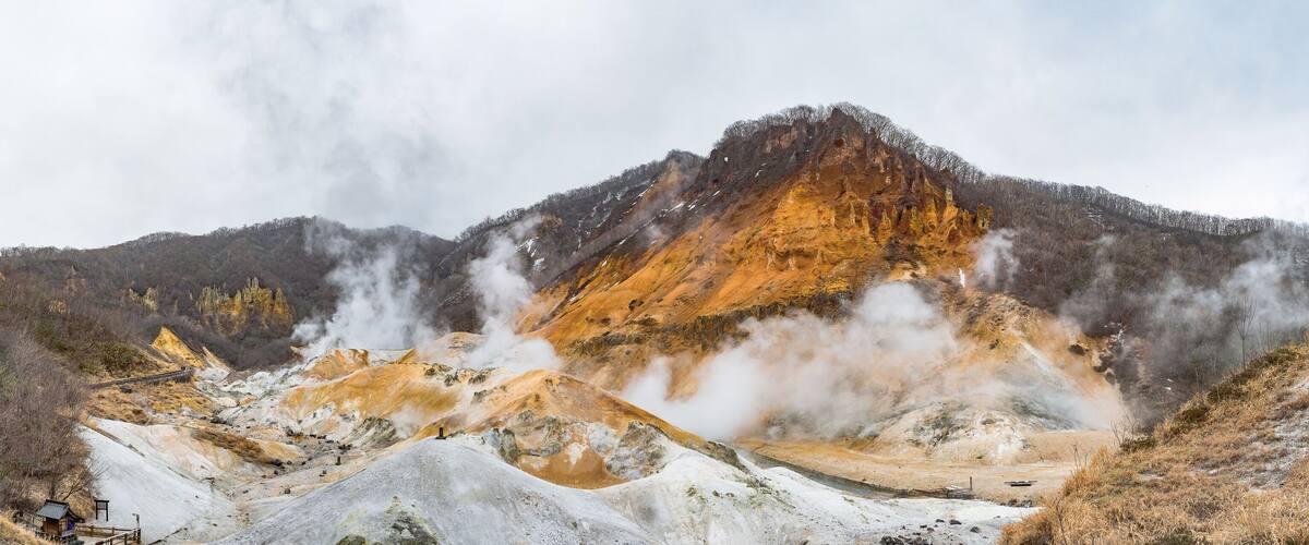 A geothermal area with steam vents, mineral deposits, and a wooden viewing platform.