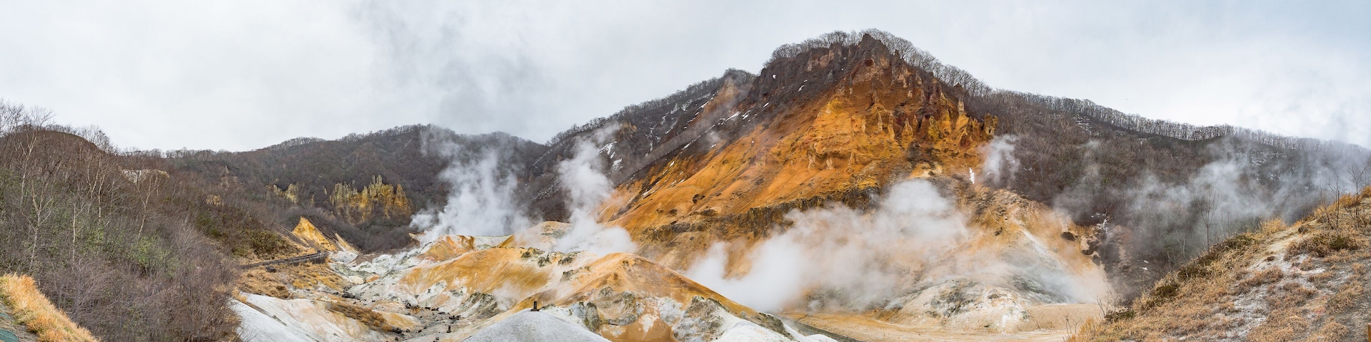 A geothermal area with steam vents, mineral deposits, and a wooden viewing platform.