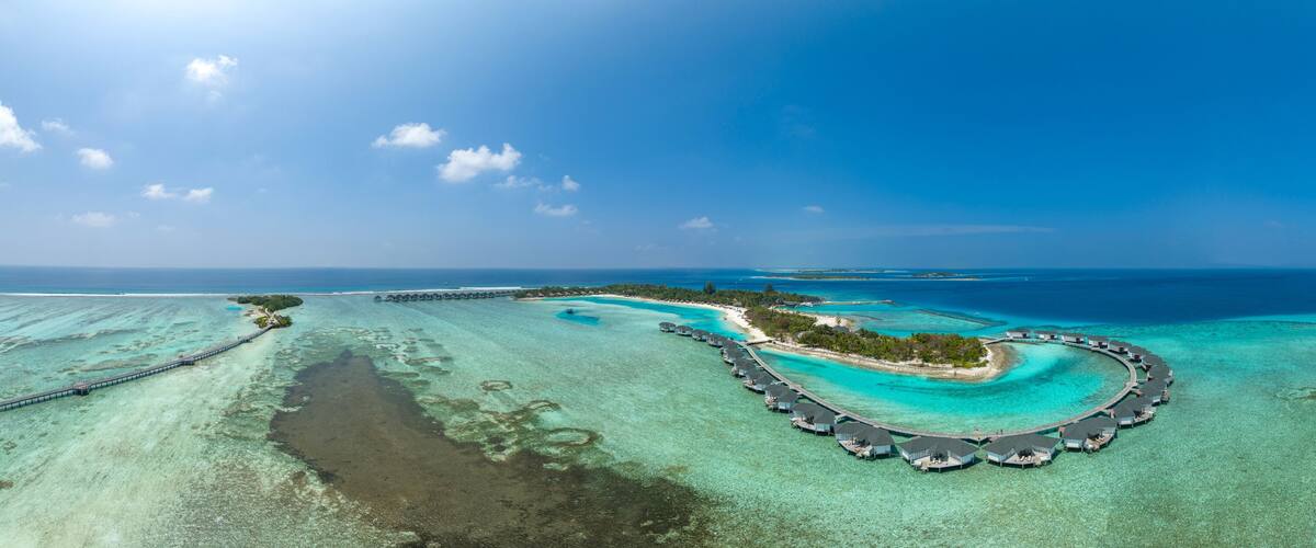 An aerial view of a tropical island resort with overwater bungalows and clear turquoise waters.