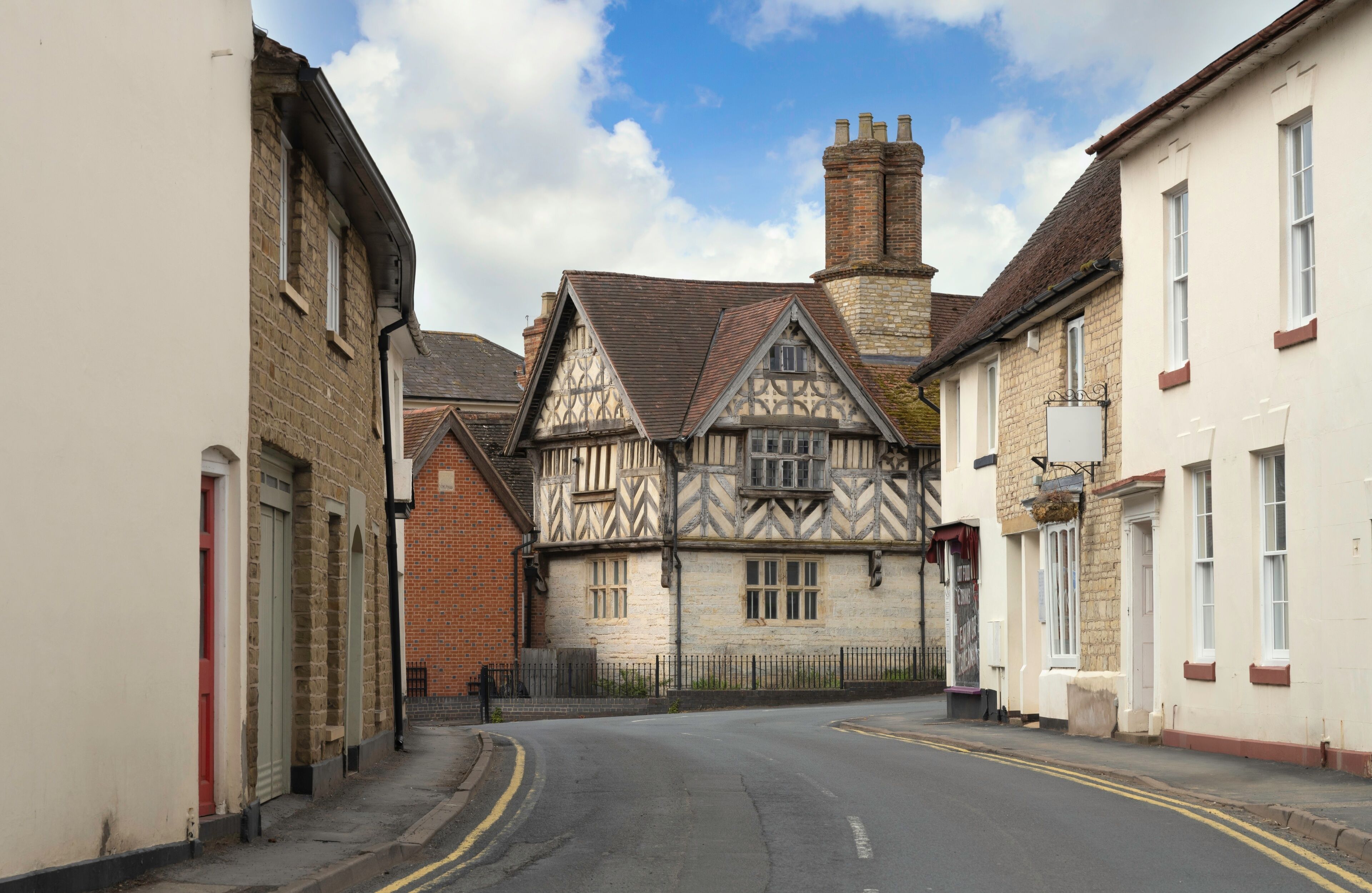 A narrow street with Tudor-style houses and a clear blue sky.
