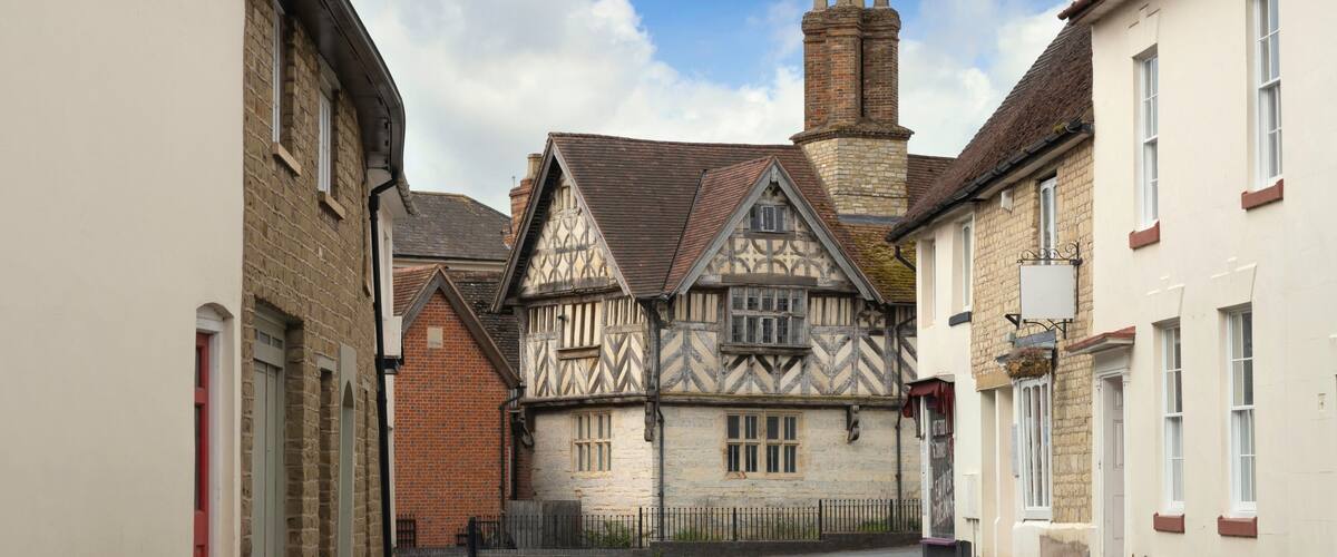 A narrow street with Tudor-style houses and a clear blue sky.