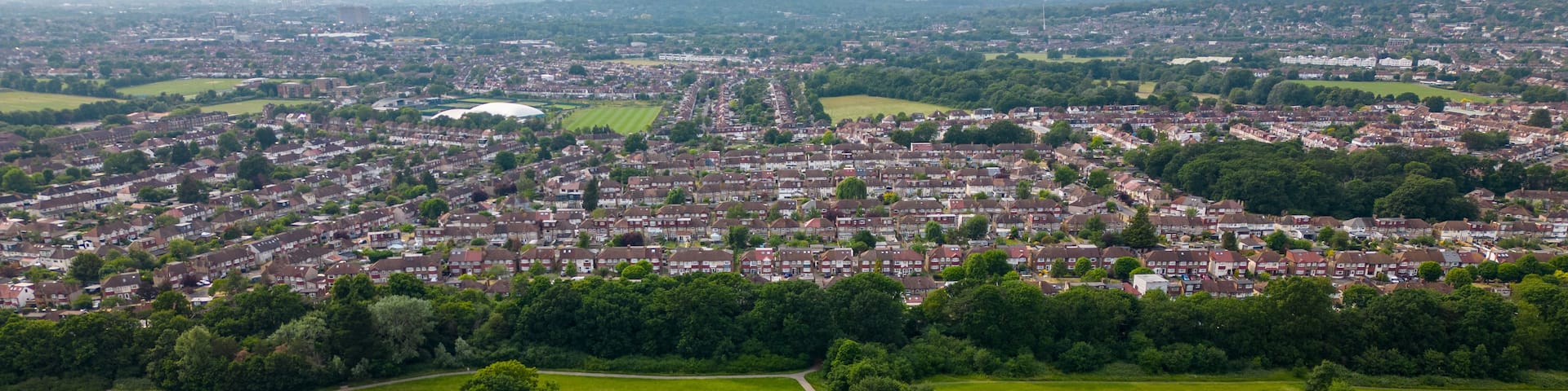 An aerial view of a residential area with houses, green fields, and a large open park.