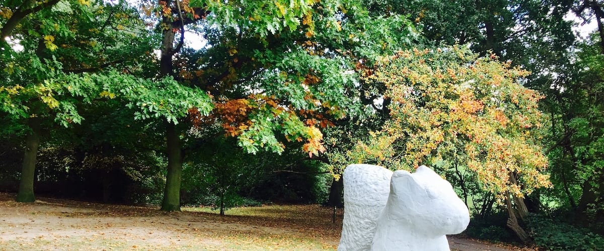 A white stone sculpture of a bear in a park.
