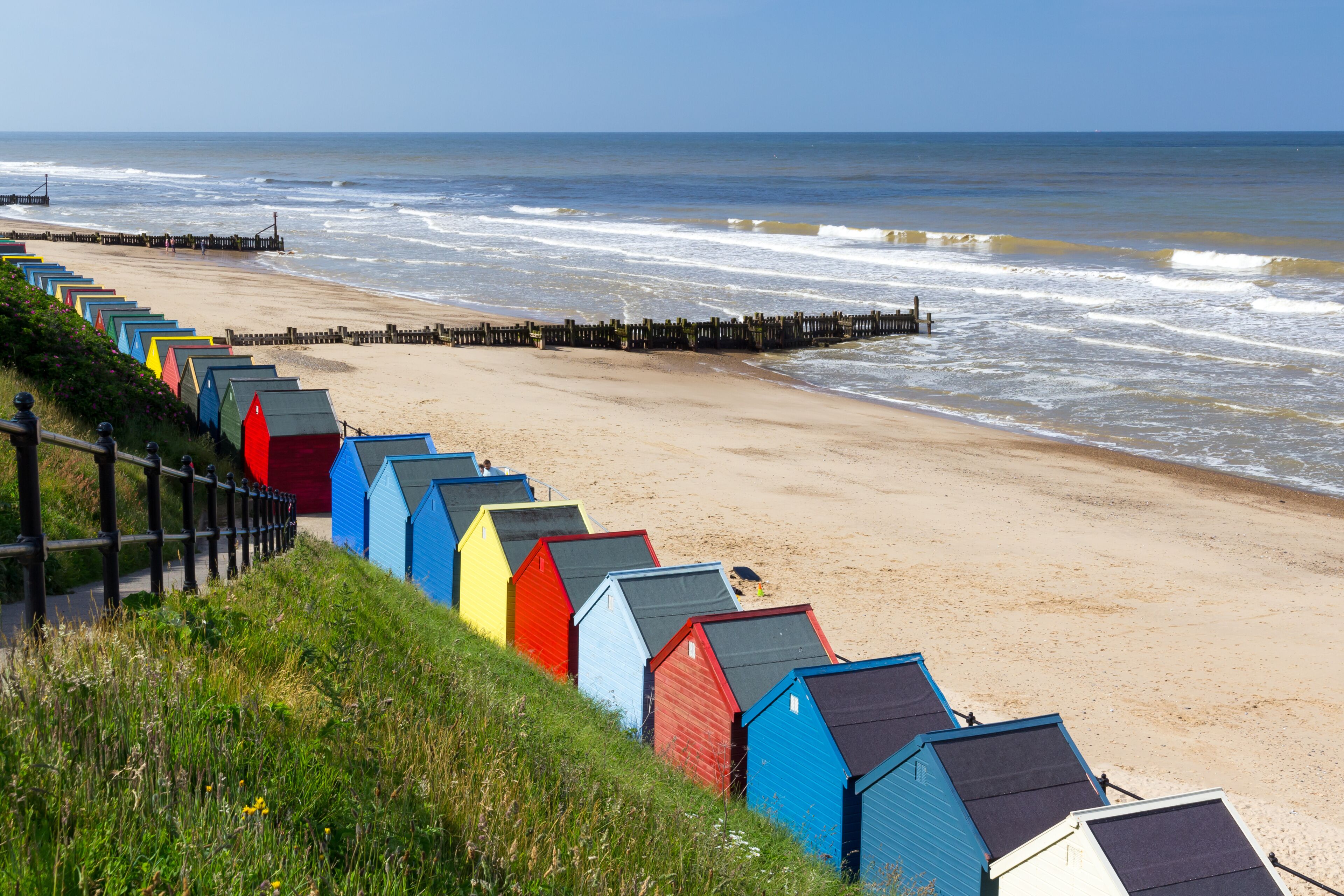 A beach with colorful beach huts and a wooden pier extending into the sea.