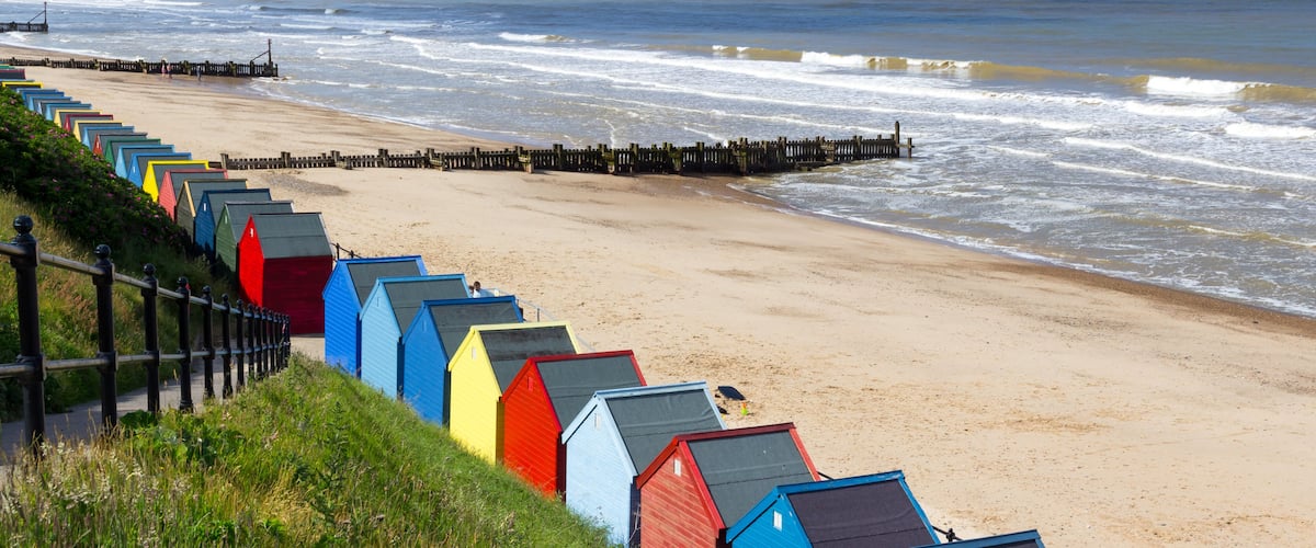 A beach with colorful beach huts and a wooden pier extending into the sea.