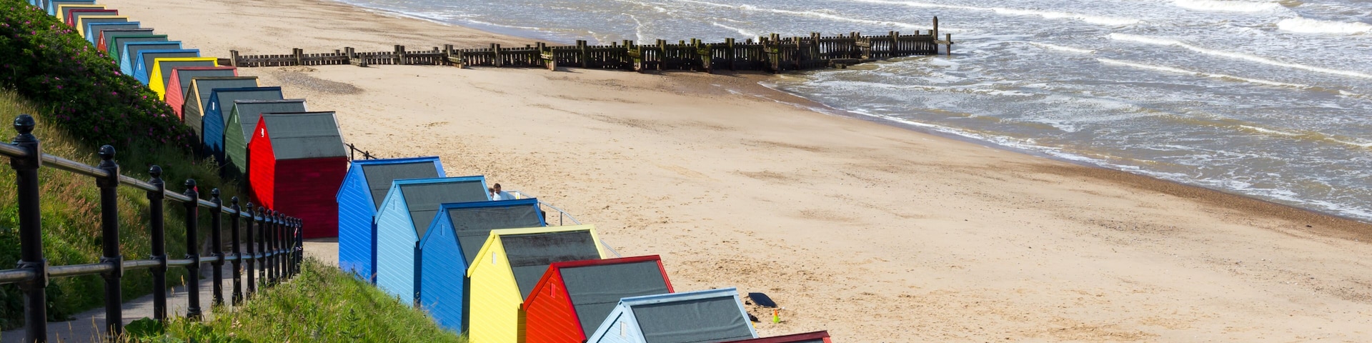 A beach with colorful beach huts and a wooden pier extending into the sea.