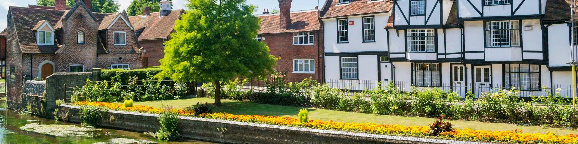 A canal with flower beds, Tudor-style houses, and a clear blue sky.