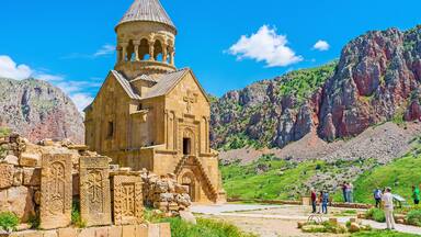 A historic church with a bell tower, surrounded by rugged mountains and a clear blue sky.