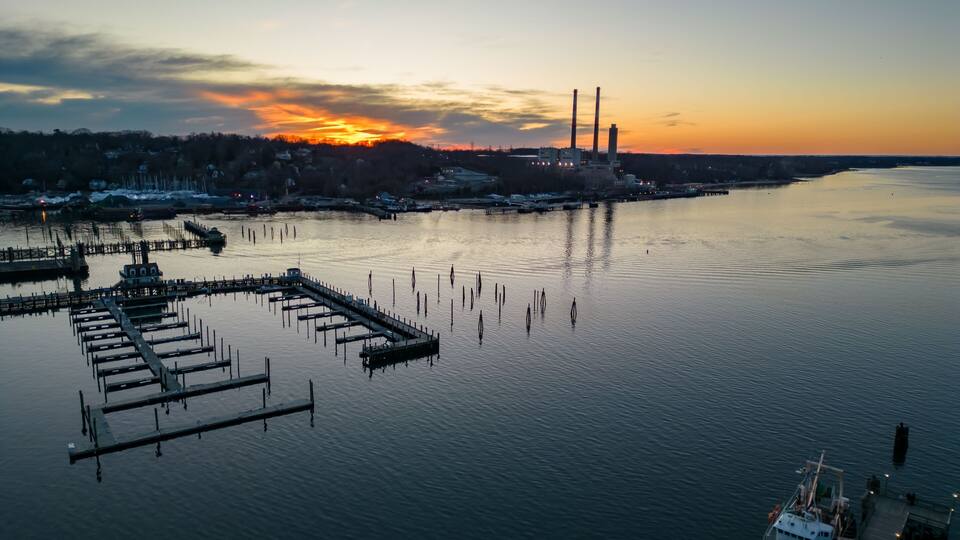 A sunset over a calm harbor with docks and a ship.