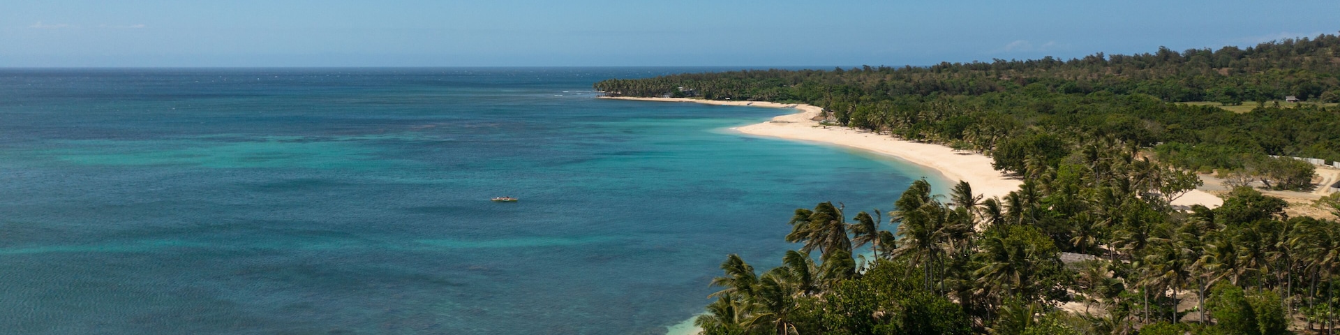 Une plage tropicale aux eaux turquoise et limpides, bordée d’un rivage sablonneux et d’une végétation luxuriante de palmiers.