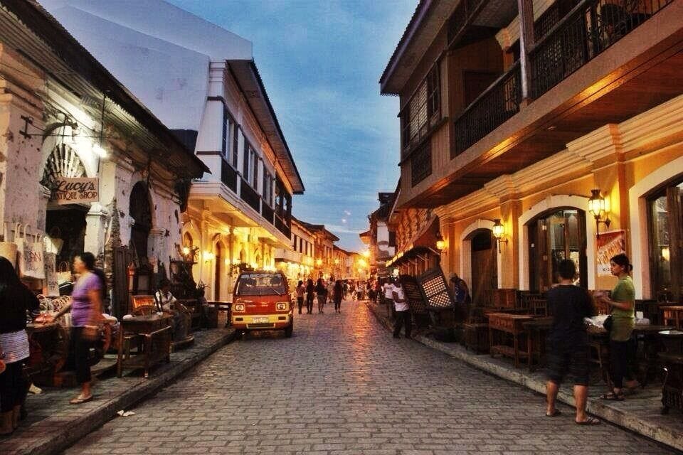 A cobblestone street lined with traditional buildings and outdoor seating, suggesting a historic or cultural area.