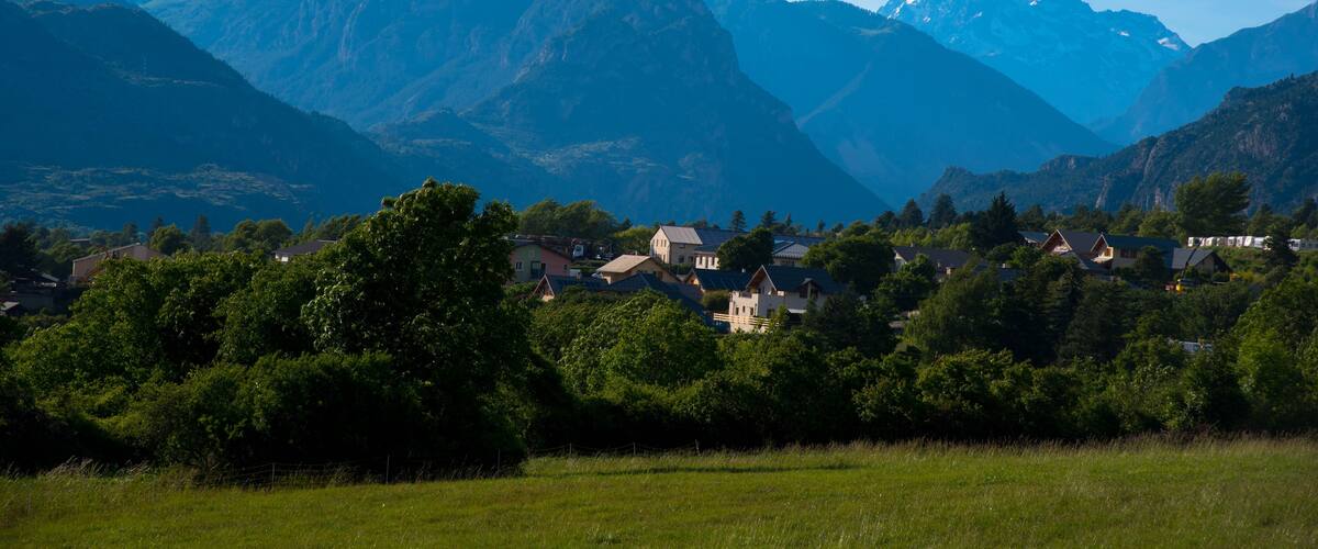 A mountain village with houses nestled among lush greenery and towering peaks.