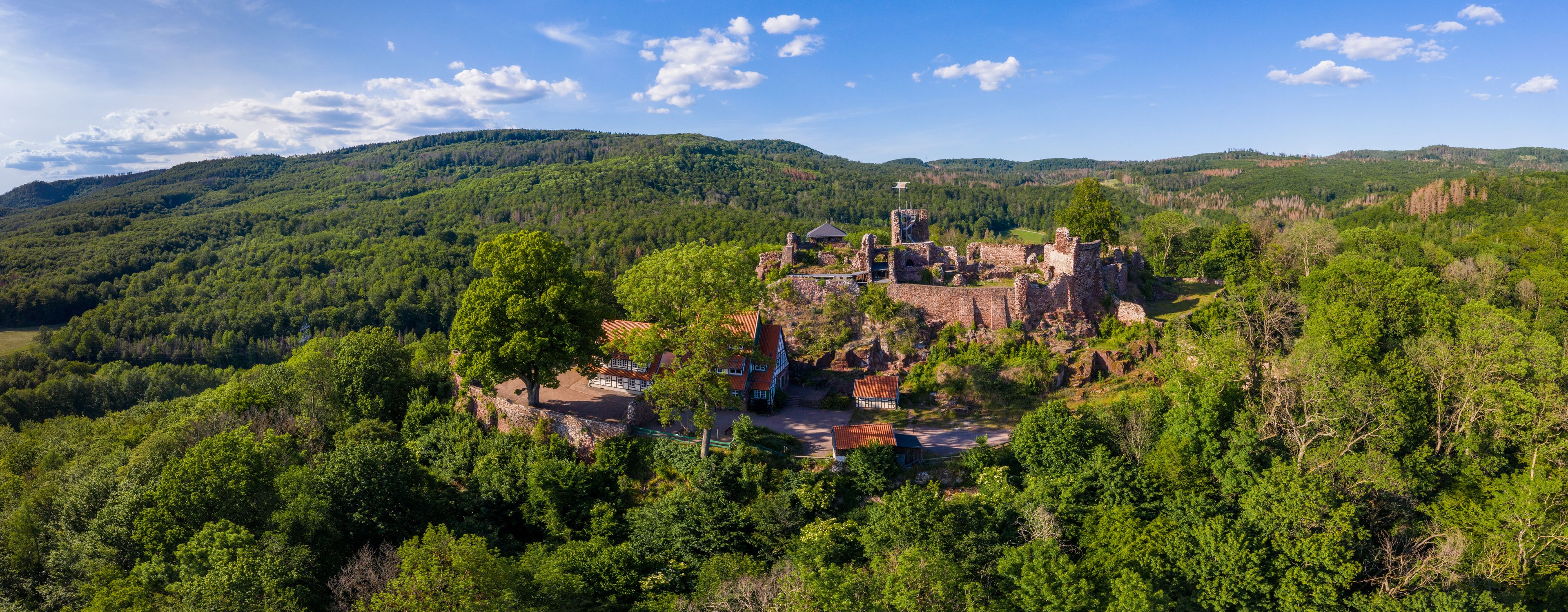 Eine historische Burgruine, umgeben von üppigem Grünwald und Hügeln.