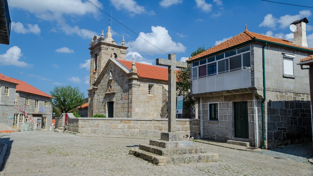 Eine Kopfsteinpflasterstraße mit einer Steinkirche und einem modernen Gebäude mit rotem Dach.