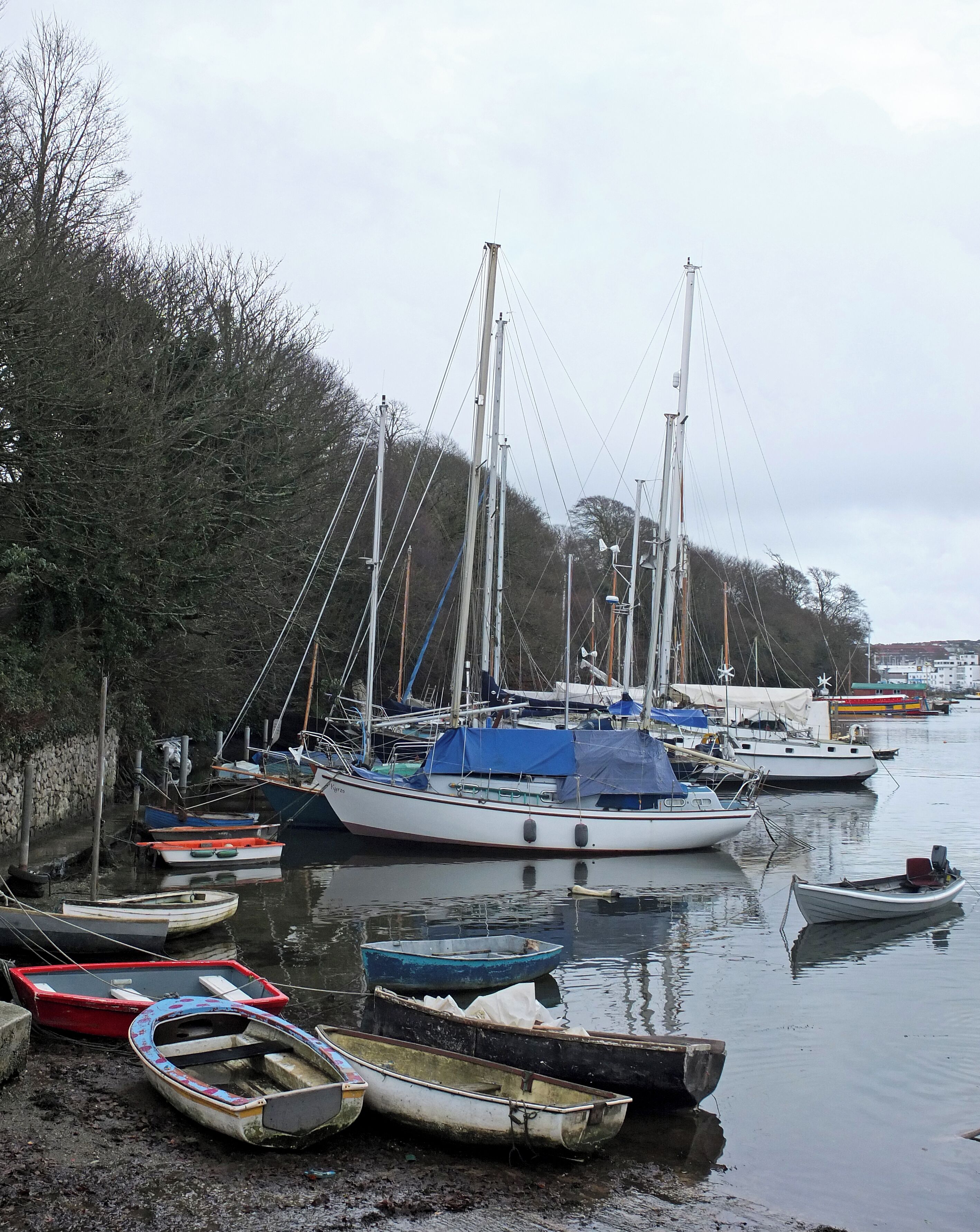 A harbor with various boats, including sailboats and smaller rowboats, docked along the shore.
