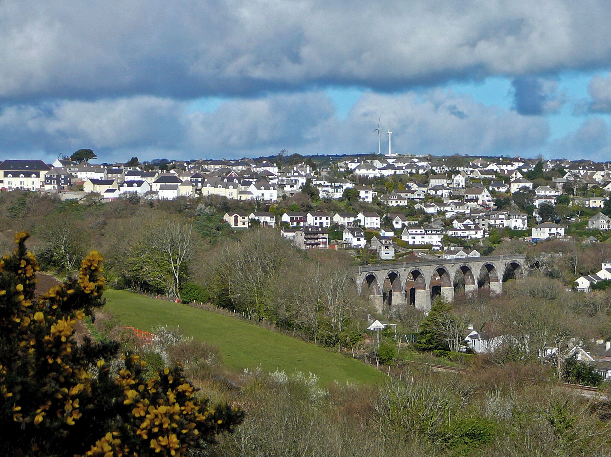 A residential area with houses, a viaduct, and wind turbines in the distance.