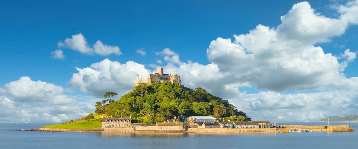 A castle on a green hill surrounded by water, with a clear sky and clouds.