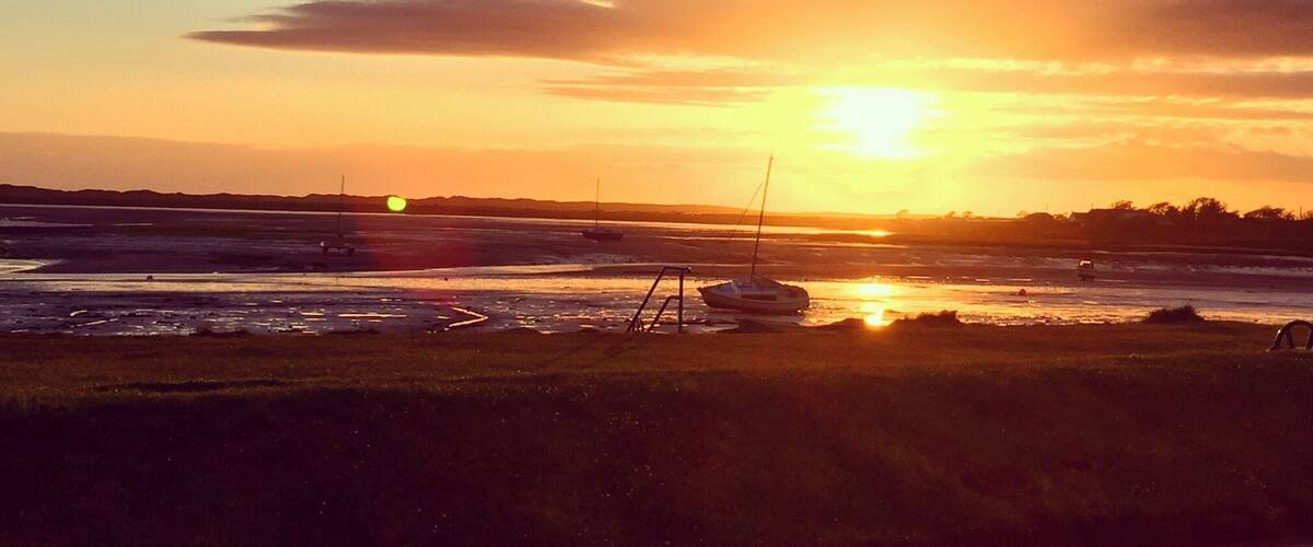 A sunset over a coastal area with boats on the water and a road in the foreground.