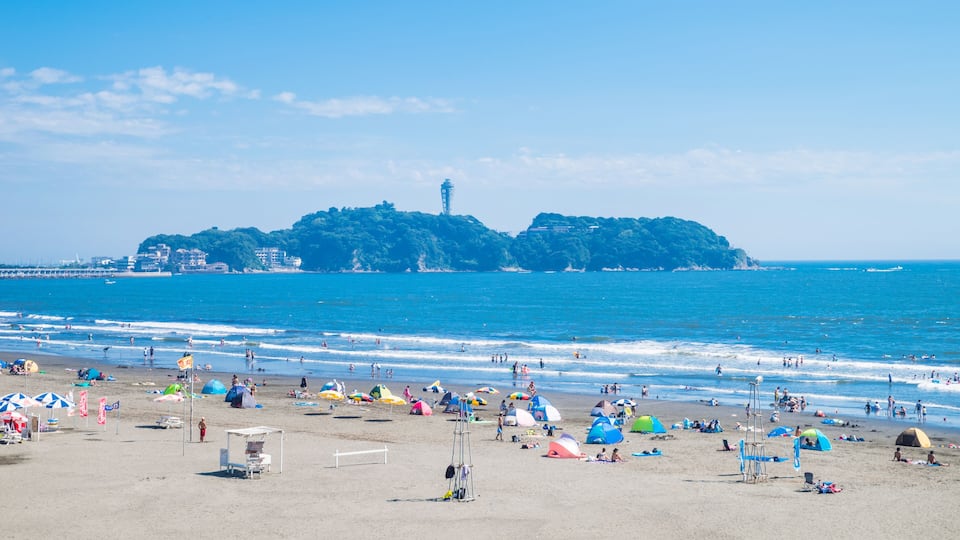 A beach with tents, umbrellas, and a lighthouse in the distance.