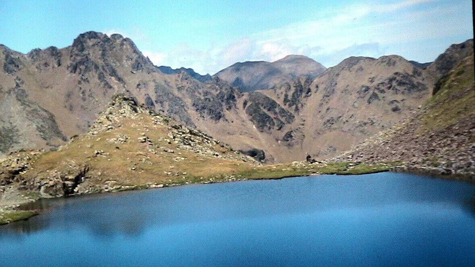 A mountain landscape with a clear blue lake surrounded by rugged peaks.