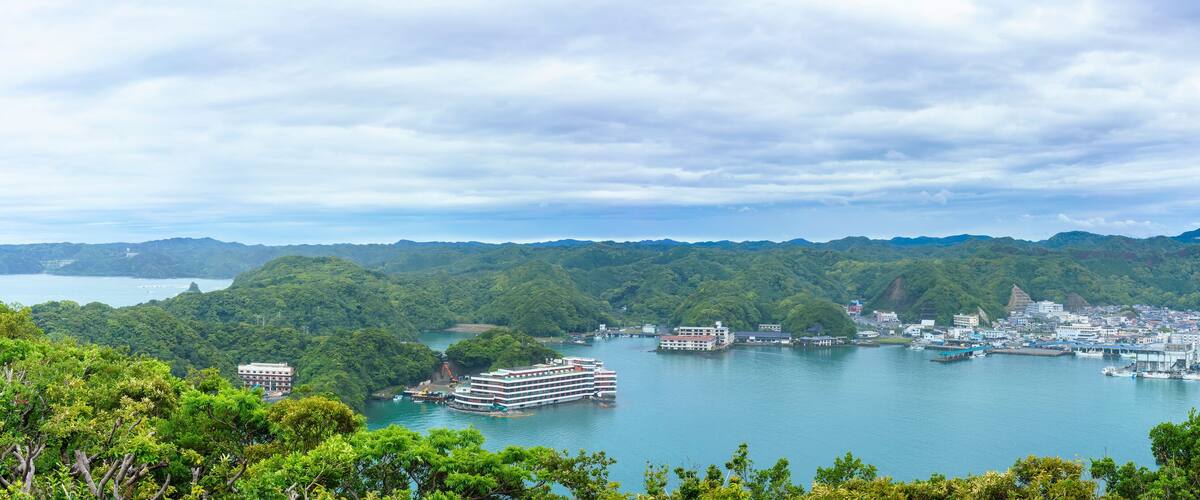 A coastal city with a harbor, surrounded by mountains and dense greenery.