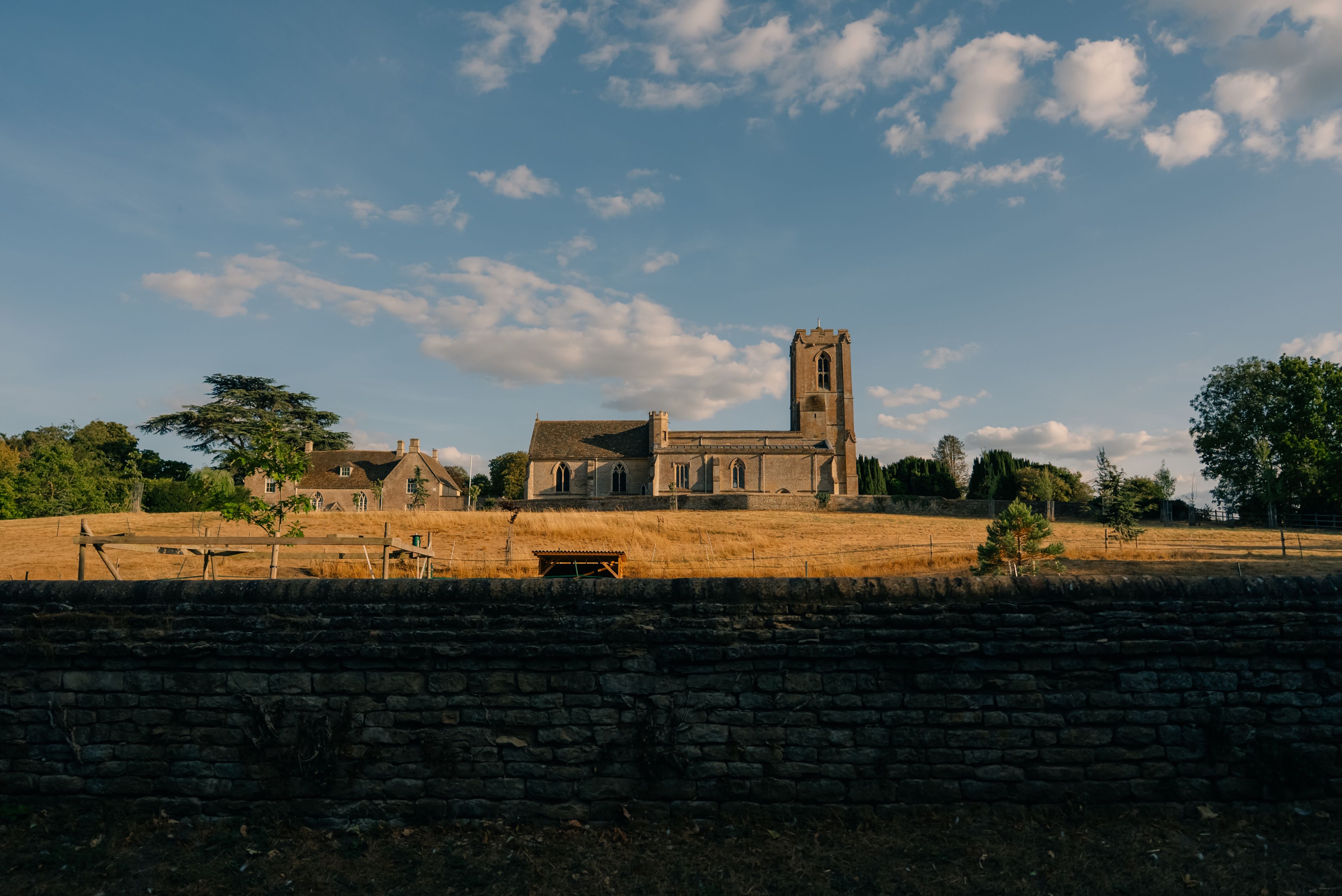 A historic church with a tall tower, surrounded by a stone wall and a grassy field.