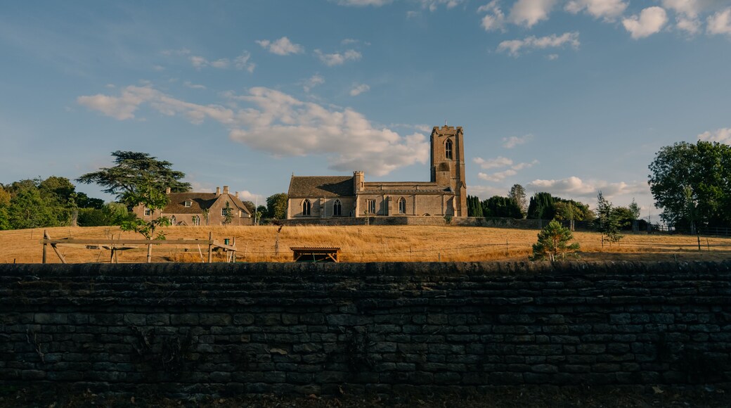 A historic church with a tall tower, surrounded by a stone wall and a grassy field.