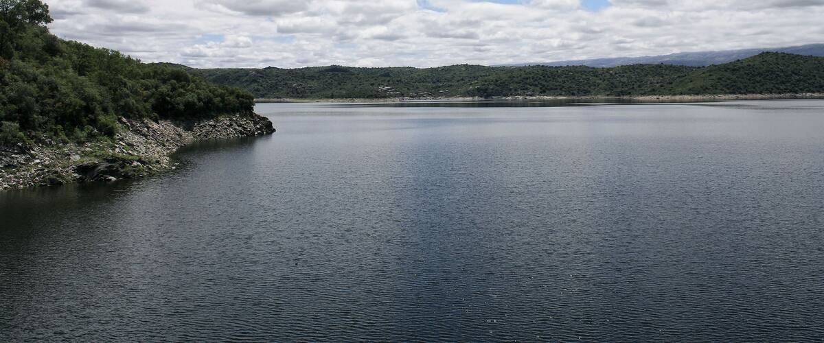 A calm lake surrounded by hills and trees under a partly cloudy sky.