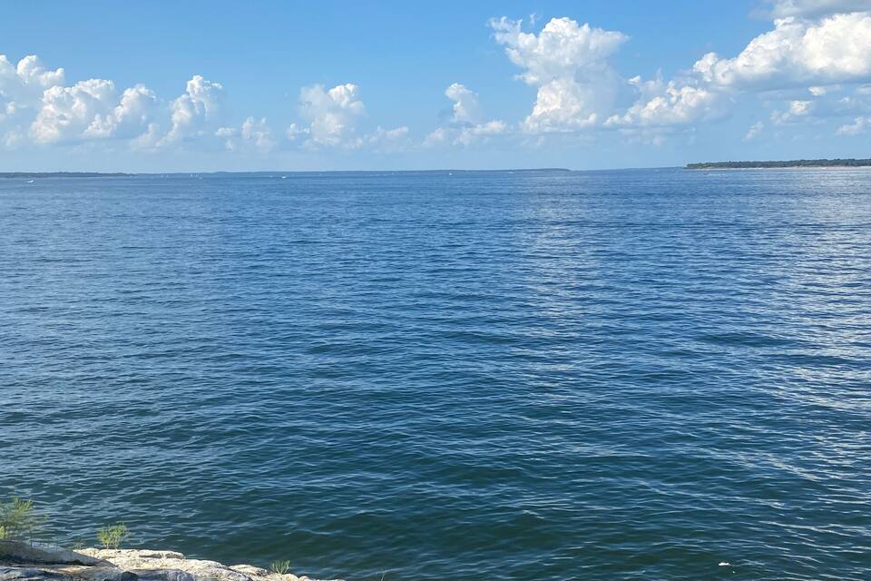 Mar tranquila con un litoral rocoso y una masa de tierra distante bajo un cielo despejado.