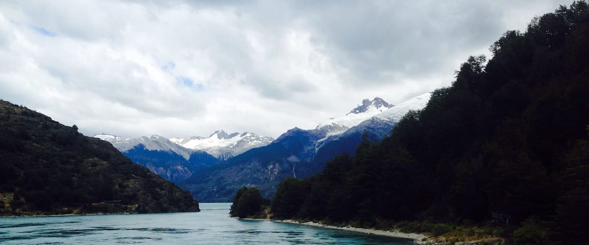 A turquoise river surrounded by mountains and dense forests.