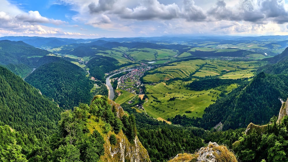 A valley with a river, surrounded by forested mountains and a small town.