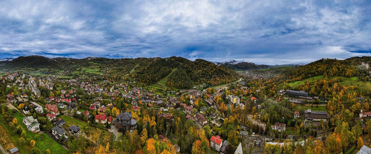 A panoramic view of a town nestled in a valley with autumn foliage, surrounded by hills and mountains.