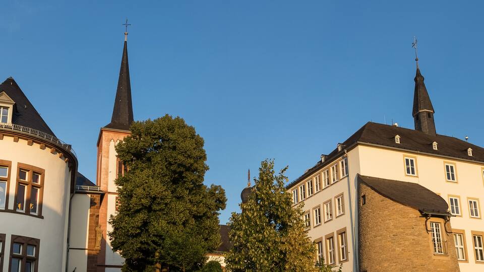 A church with a tall spire and a round tower, surrounded by trees and other buildings.