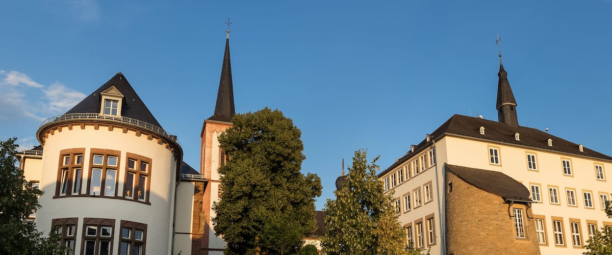 A church with a tall spire and a round tower, surrounded by trees and other buildings.