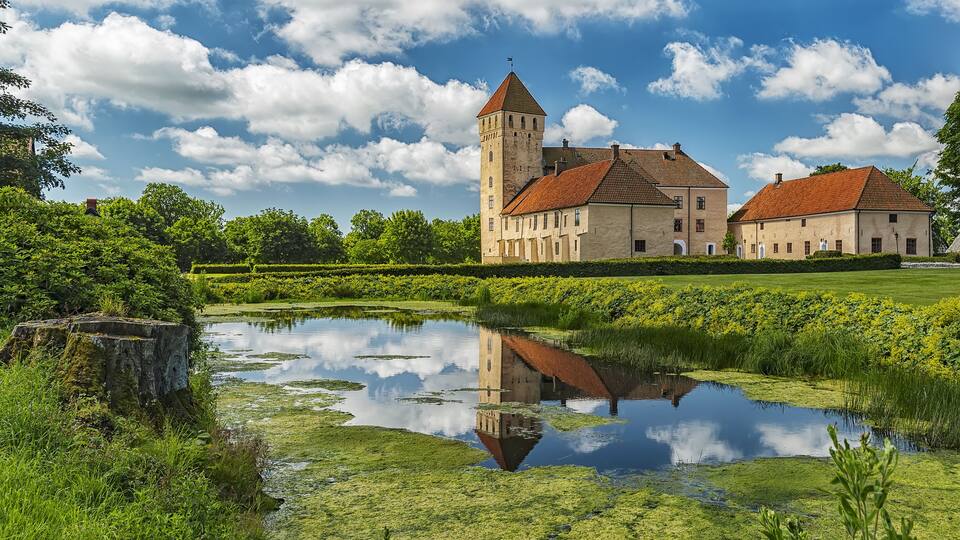 A historic building with a tower, surrounded by a pond and lush greenery.