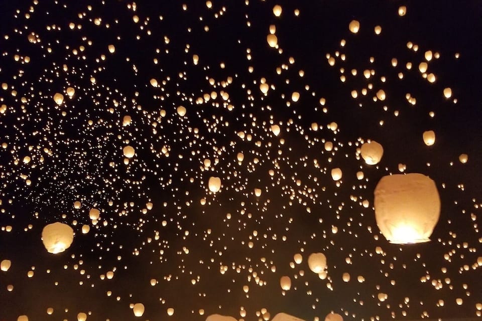 Una multitud liberando linternas al cielo de noche.