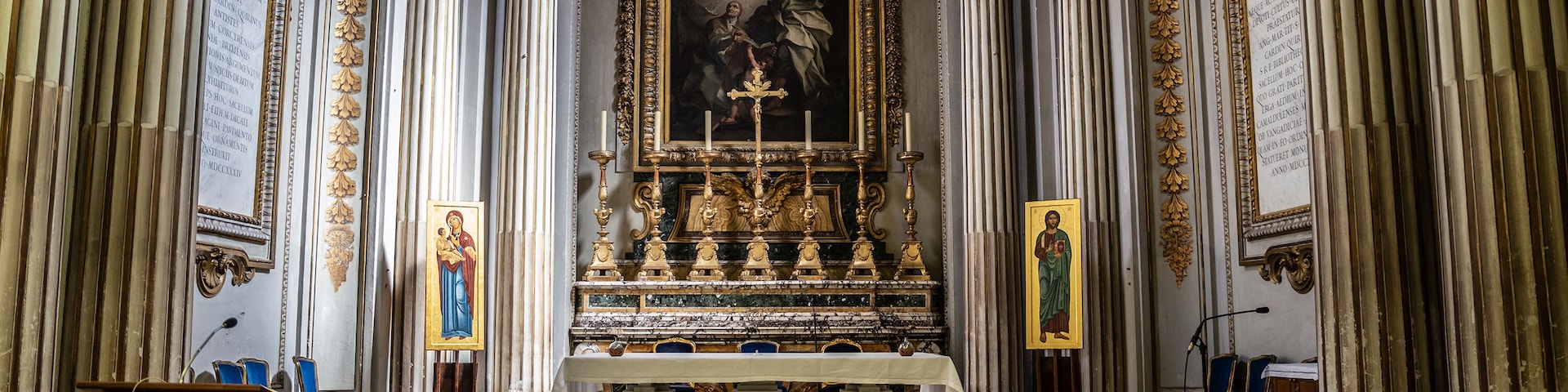 An ornate church interior with a central altar, gold decorations, and a large religious painting.
