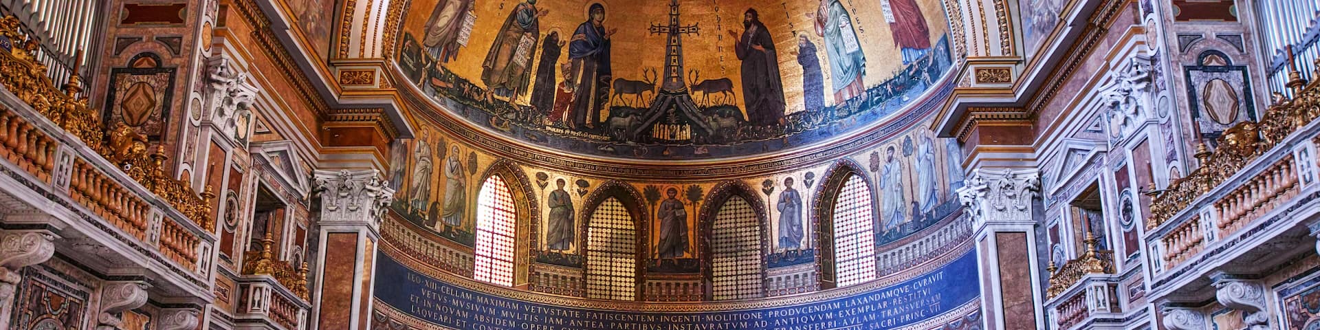 An ornate church interior with detailed frescoes, a central dome, and a prominent cross.
